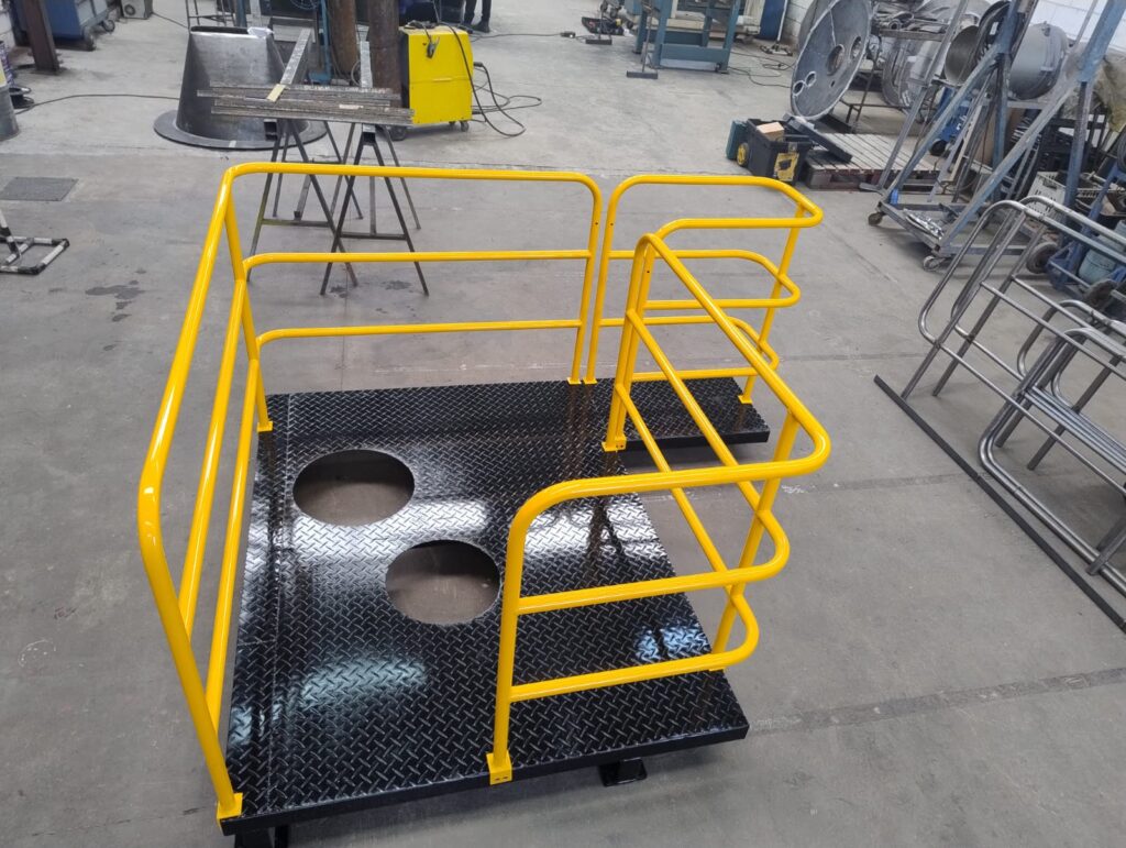 Sugestão de Alt Text: Plataforma e estrutura metálica com pintura industrial amarela e piso xadrez